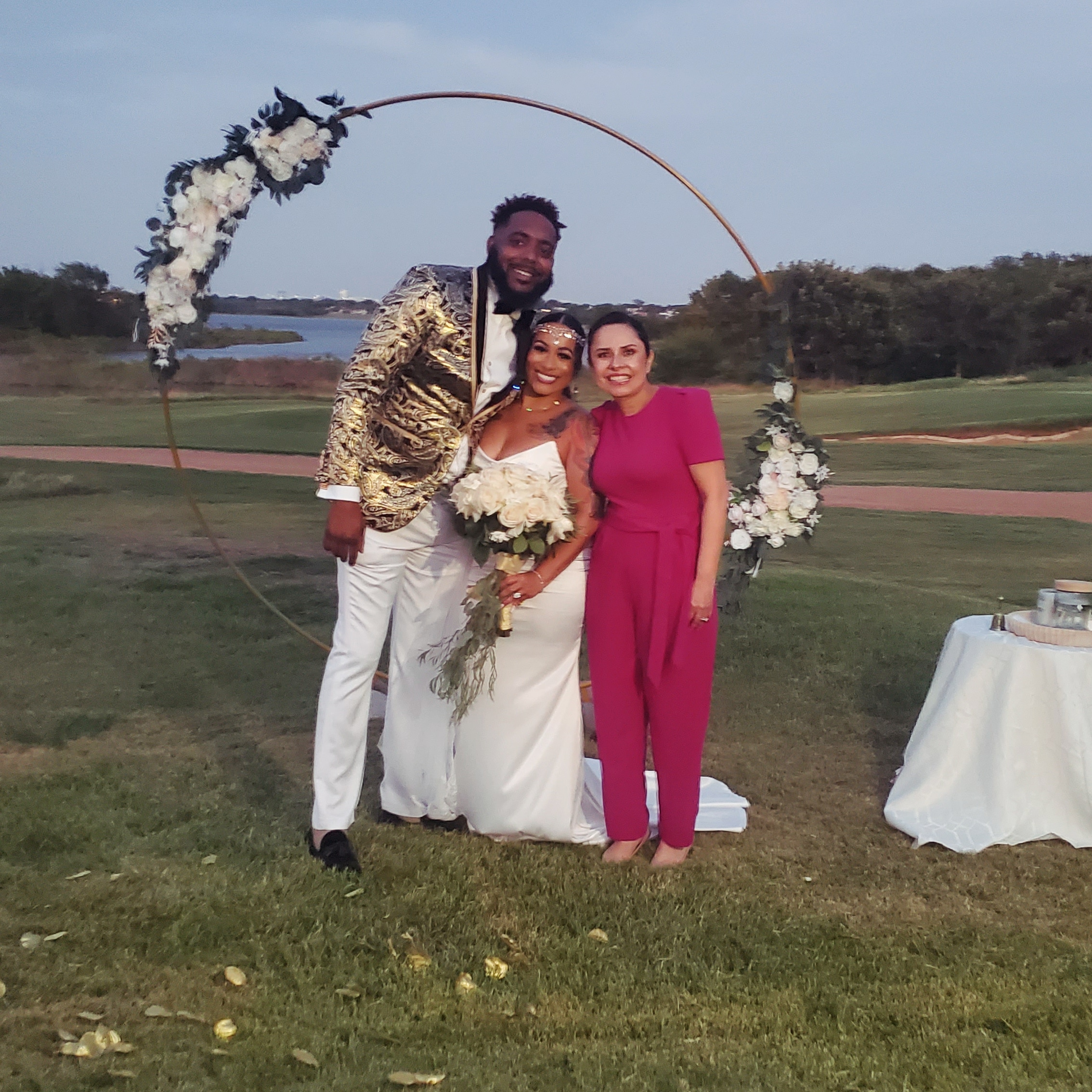 Pareja de novios y oficiante bajo un arco decorado con flores