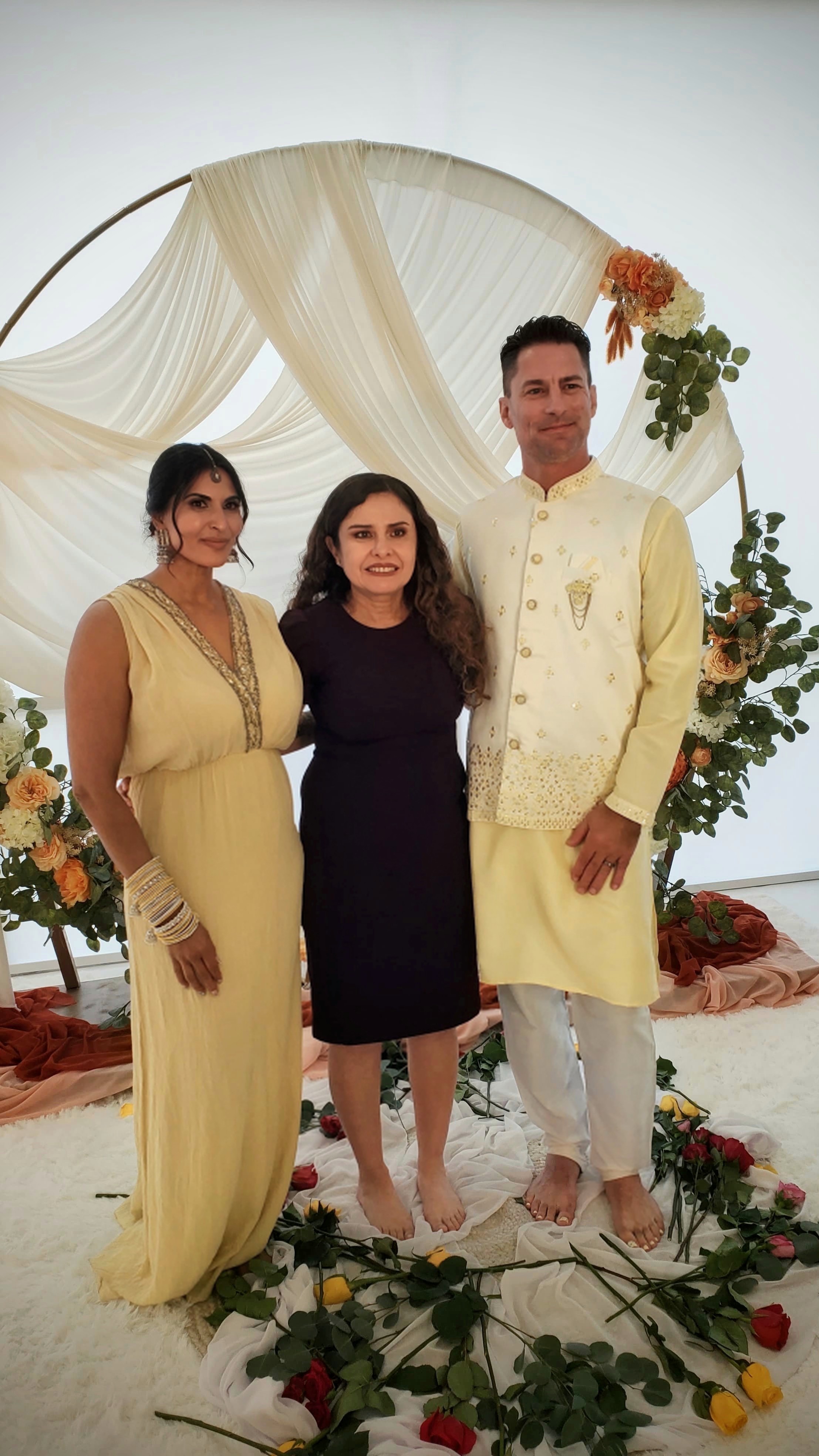Pareja y oficiante bajo un arco ceremonial con telas y decoración floral