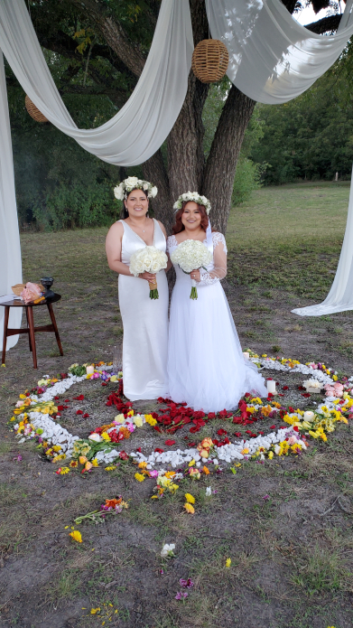 Two brides standing inside heart-shaped floral arrangement during outdoor Mayan wedding ceremony