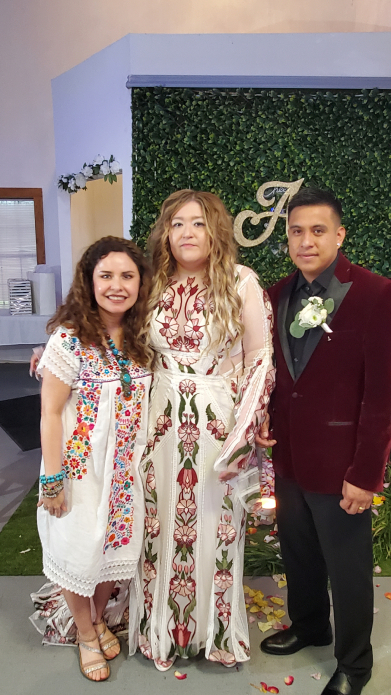 Wedding couple and oficiant posing in front of greenery wall with Mayan ceremony decor