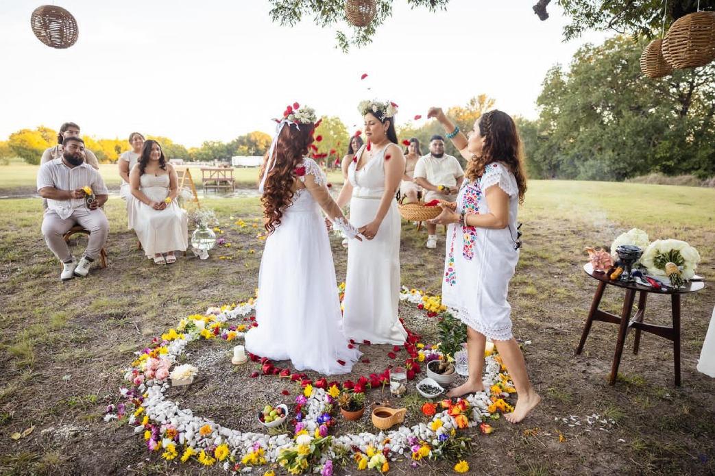 Oficiant conducting outdoor Mayan wedding ceremony with couple exchanging vows surrounded by guests and flowers